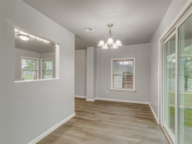 unfurnished dining area with baseboards, a notable chandelier, wood finished floors, and visible vents