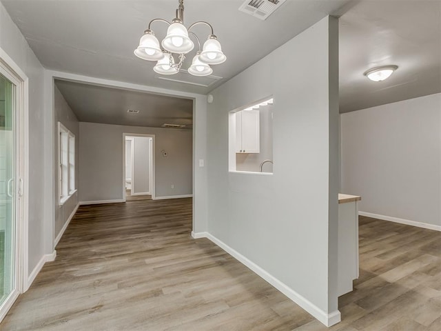 unfurnished dining area featuring baseboards, light wood-type flooring, a chandelier, and visible vents