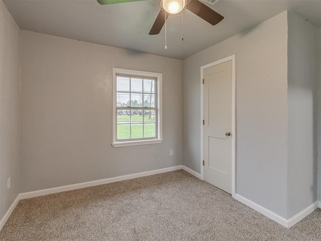 spare room featuring light colored carpet, a ceiling fan, and baseboards