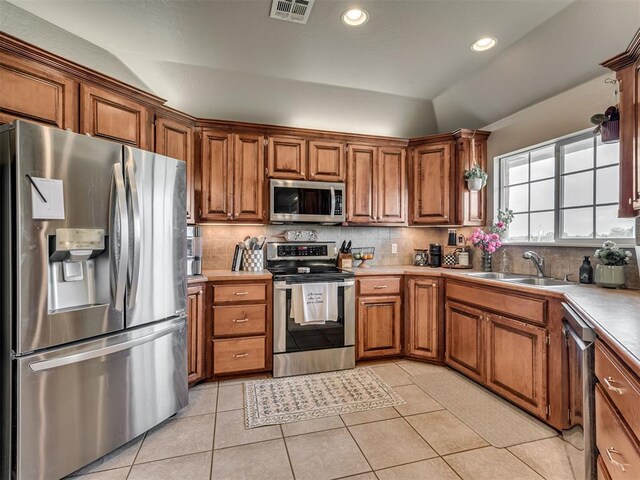 kitchen featuring a sink, brown cabinetry, stainless steel appliances, decorative backsplash, and visible vents