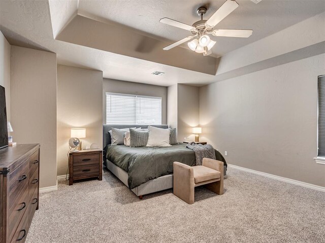 bedroom featuring light colored carpet, a ceiling fan, baseboards, a tray ceiling, and visible vents