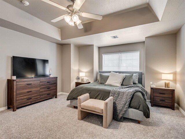 bedroom featuring visible vents, baseboards, light colored carpet, a tray ceiling, and a ceiling fan
