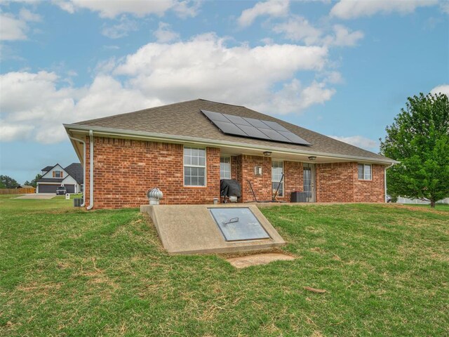 back of house featuring solar panels, a lawn, brick siding, cooling unit, and a shingled roof