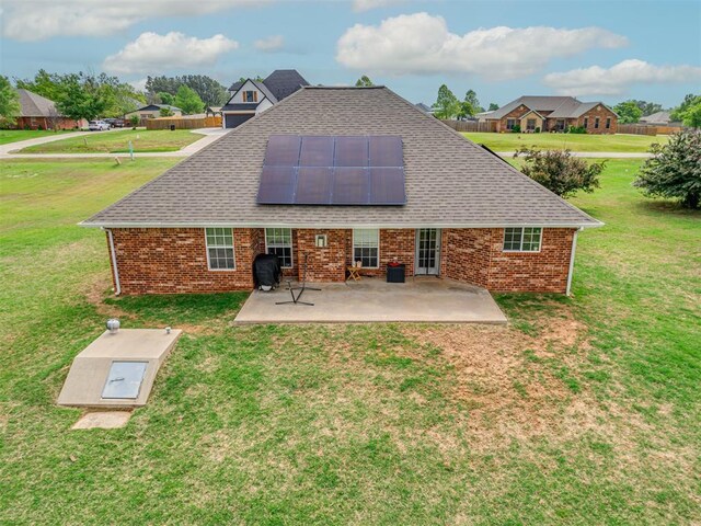 back of property with a lawn, roof mounted solar panels, roof with shingles, and brick siding
