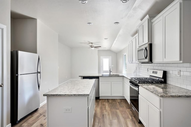 kitchen featuring a sink, a peninsula, a ceiling fan, light wood-style flooring, and appliances with stainless steel finishes