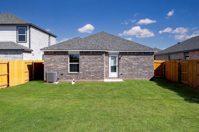 rear view of house featuring a shingled roof, central AC, brick siding, a fenced backyard, and a lawn
