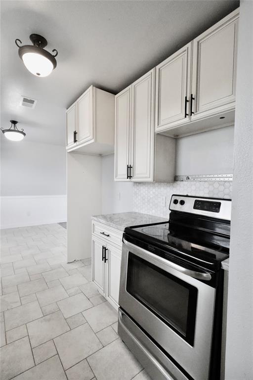 kitchen featuring stainless steel electric stove, tasteful backsplash, white cabinets, and light stone countertops