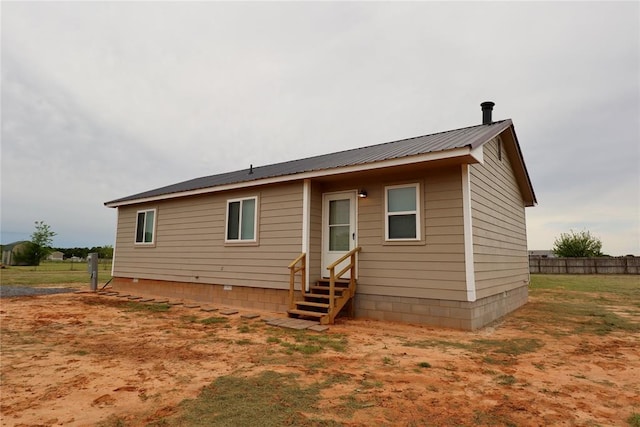 rear view of house featuring entry steps, fence, and metal roof