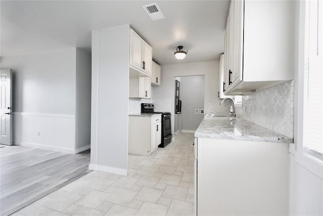 kitchen with black electric range, a sink, decorative backsplash, light stone counters, and white cabinetry
