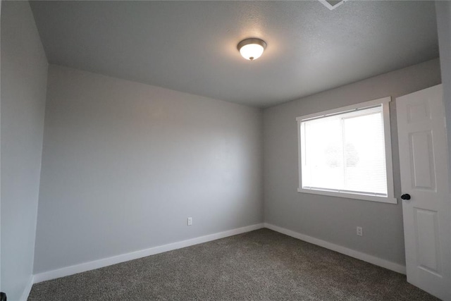 spare room featuring dark colored carpet and baseboards