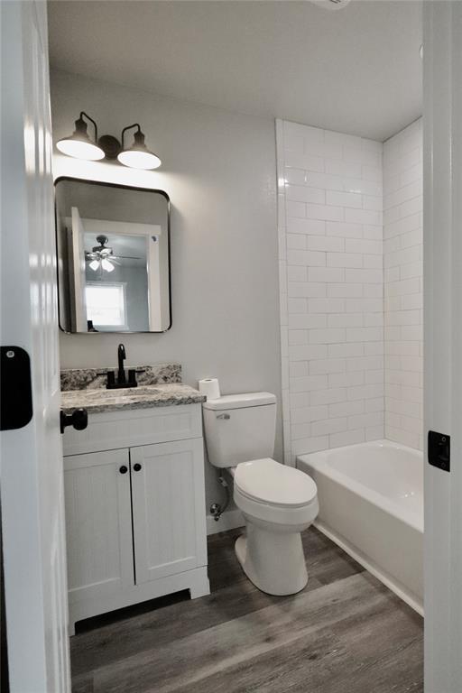 full bath with wood finished floors, toilet, vanity, shower / bath combination, and a ceiling fan