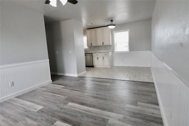 kitchen featuring wainscoting, stainless steel dishwasher, a ceiling fan, light wood-style flooring, and white cabinets