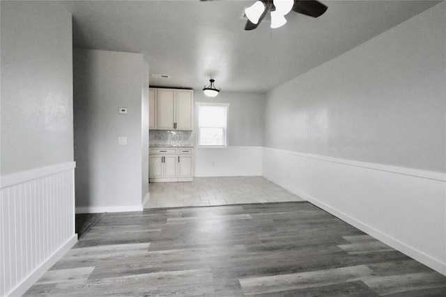 unfurnished dining area featuring ceiling fan, wood finished floors, and wainscoting