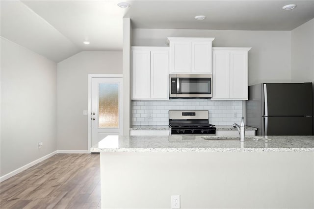 kitchen featuring decorative backsplash, light stone countertops, light wood-type flooring, white cabinets, and appliances with stainless steel finishes