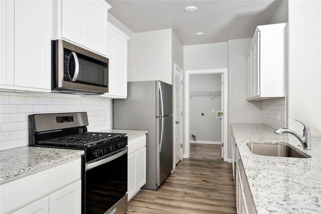 kitchen featuring white cabinets, appliances with stainless steel finishes, a sink, decorative backsplash, and light wood-type flooring