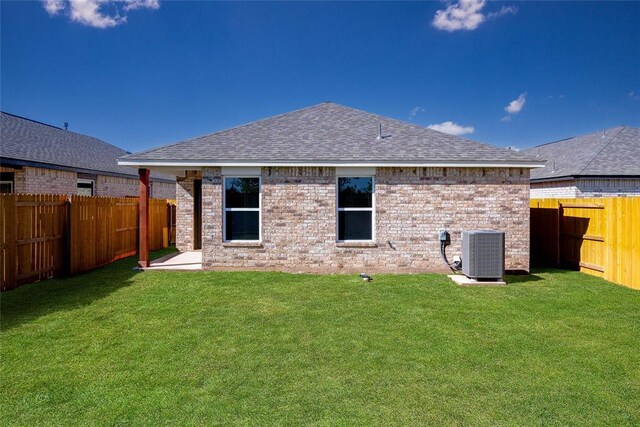 back of property with a shingled roof, brick siding, a fenced backyard, central air condition unit, and a lawn