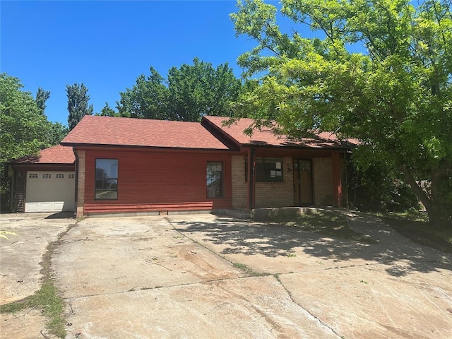 single story home with an attached garage, a shingled roof, and concrete driveway
