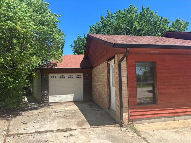 view of side of property featuring a shingled roof, an attached garage, and concrete driveway