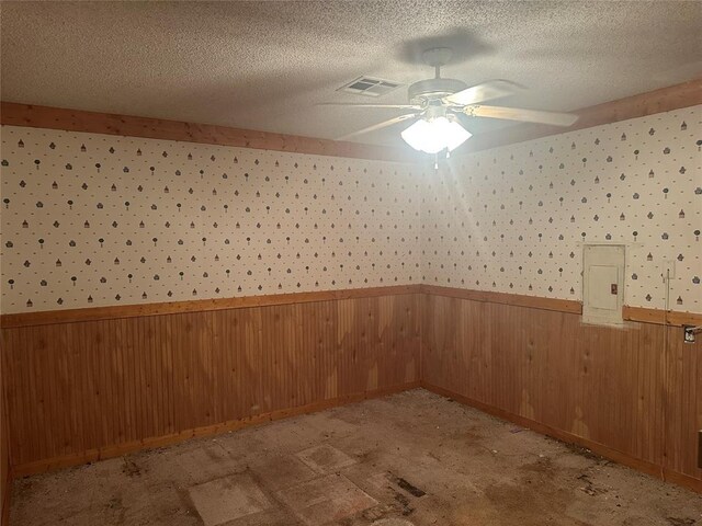 empty room featuring a textured ceiling, ceiling fan, wainscoting, and electric panel