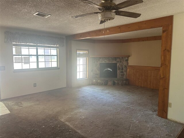 unfurnished living room featuring a ceiling fan, a textured ceiling, visible vents, wainscoting, and carpet floors