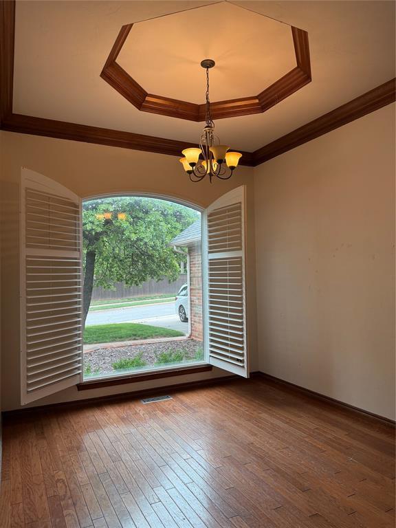 3900 Chickasha, Edmond, OK 73013 - spare room with crown molding, a tray ceiling, dark wood-type flooring, and a chandelier