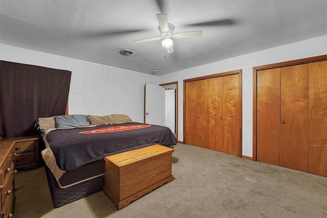 carpeted bedroom with two closets, a textured ceiling, ceiling fan, and visible vents