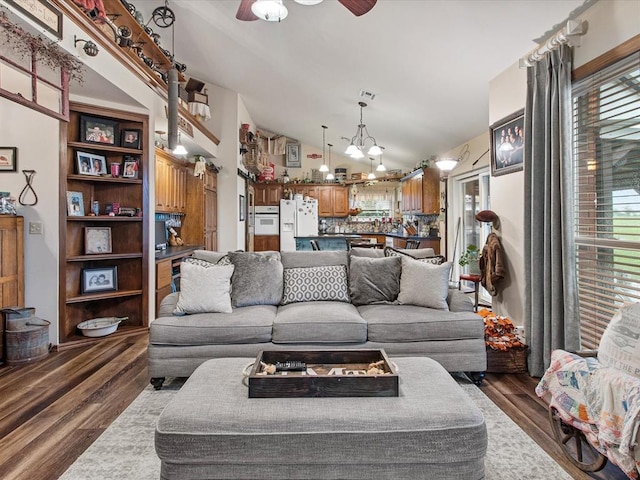 living area featuring dark wood finished floors, ceiling fan with notable chandelier, and lofted ceiling
