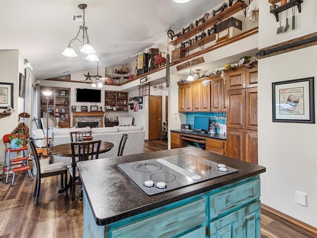 kitchen featuring dark countertops, stovetop with downdraft, a fireplace, lofted ceiling, and dark wood-type flooring