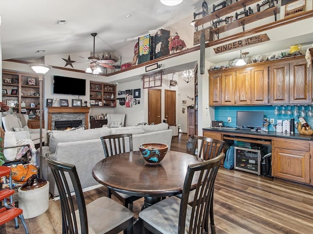dining area with ceiling fan, a fireplace, wood finished floors, lofted ceiling, and visible vents