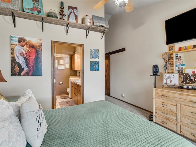 bedroom featuring ceiling fan, ensuite bathroom, light carpet, and a barn door
