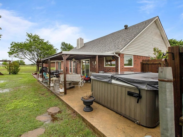 back of house featuring a patio area, a hot tub, brick siding, a yard, and a shingled roof