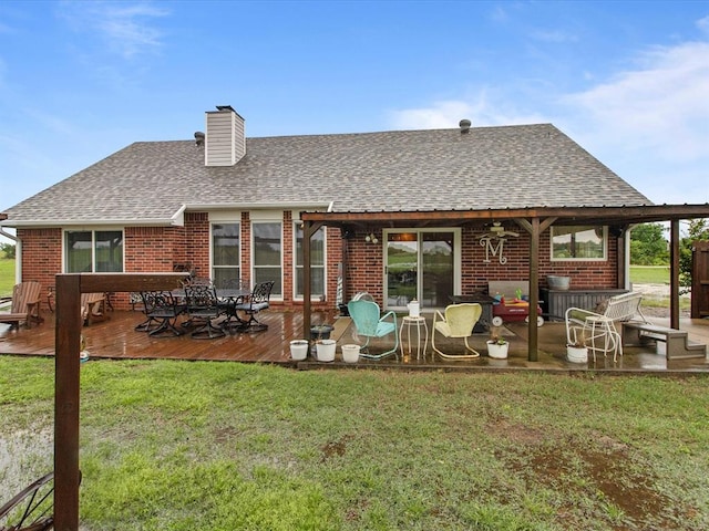 rear view of property with brick siding, a deck, a yard, and a shingled roof