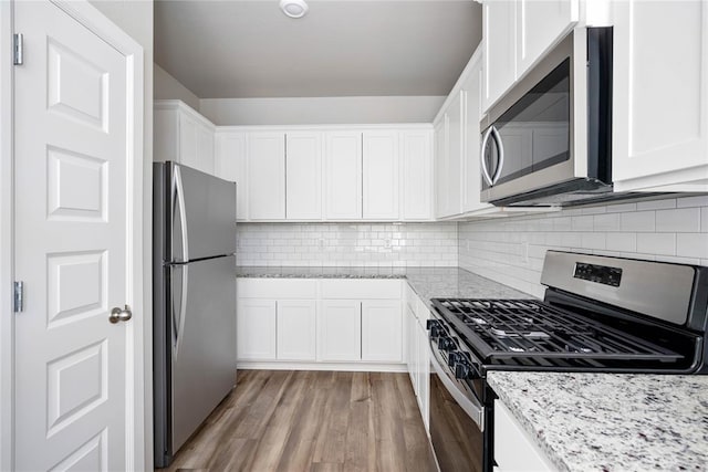 kitchen featuring white cabinets, appliances with stainless steel finishes, light stone counters, light wood-style flooring, and decorative backsplash