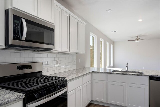 kitchen featuring white cabinets, a sink, stainless steel appliances, a ceiling fan, and decorative backsplash