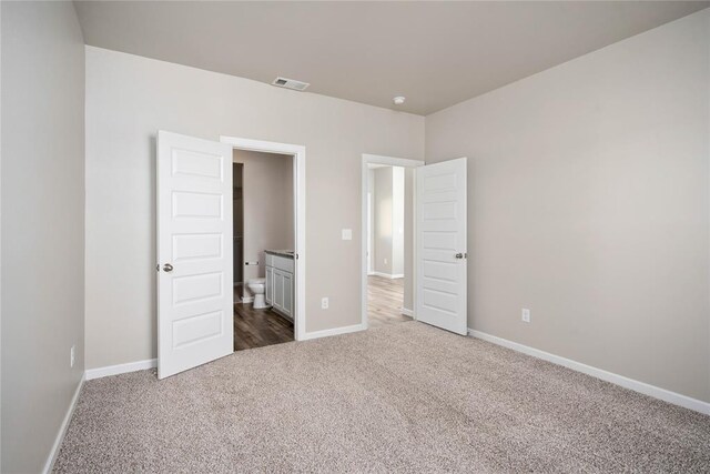 unfurnished bedroom featuring dark carpet, connected bathroom, baseboards, and visible vents