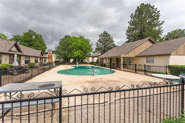 community pool with a patio, fence, and a residential view