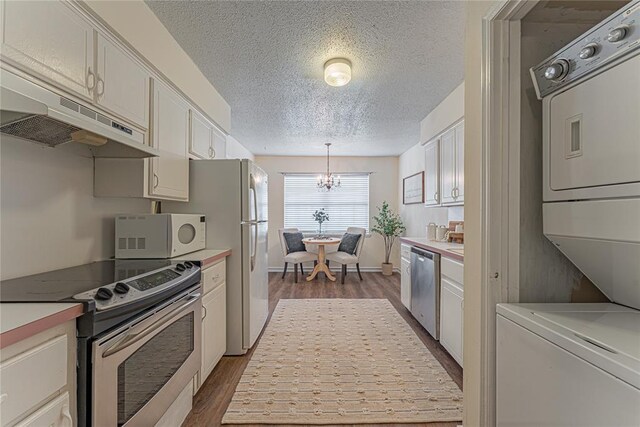 kitchen featuring stacked washer and clothes dryer, a textured ceiling, under cabinet range hood, a chandelier, and stainless steel appliances