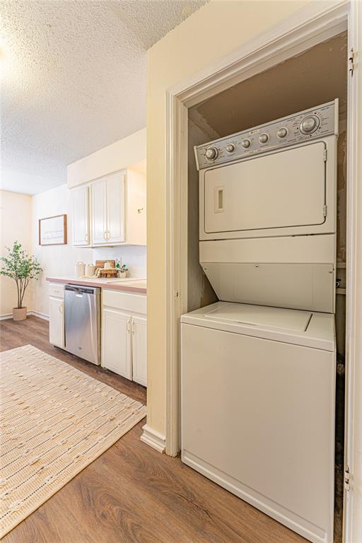 laundry room with stacked washer and clothes dryer, a textured ceiling, and wood finished floors