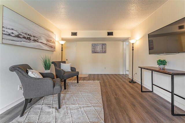 living area featuring baseboards, a textured ceiling, visible vents, and wood finished floors
