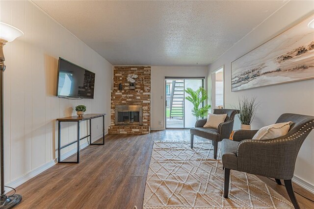 living room featuring a textured ceiling, baseboards, a brick fireplace, and wood finished floors