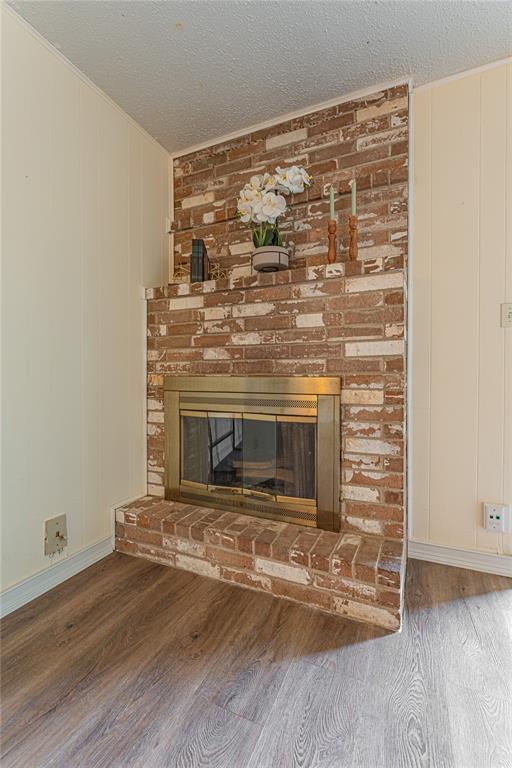 details with a brick fireplace, a textured ceiling, baseboards, and wood finished floors