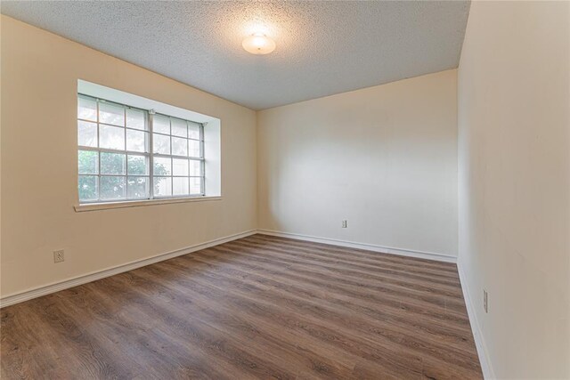 empty room with a textured ceiling, dark wood finished floors, and baseboards