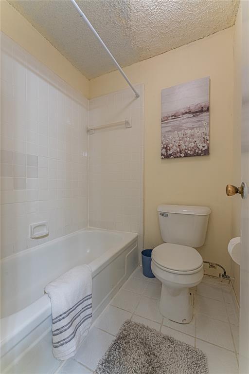 full bath featuring a textured ceiling, tile patterned floors, bathing tub / shower combination, and toilet
