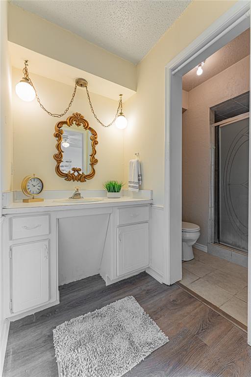 bathroom featuring vanity, toilet, a textured ceiling, wood finished floors, and a stall shower