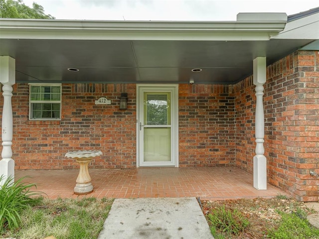 view of exterior entry with a patio and brick siding