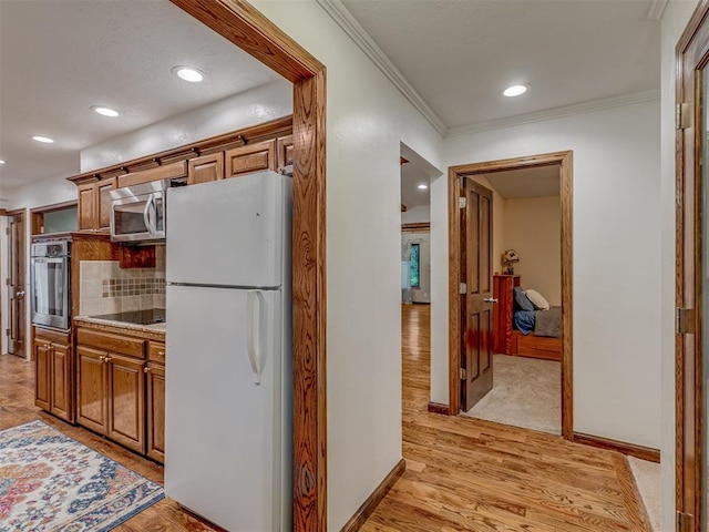 kitchen featuring decorative backsplash, brown cabinetry, crown molding, appliances with stainless steel finishes, and light wood-style flooring
