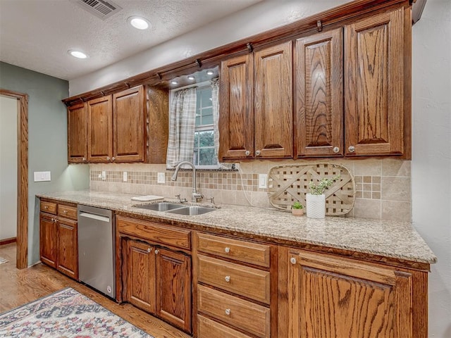 kitchen featuring stainless steel dishwasher, decorative backsplash, visible vents, brown cabinets, and a sink