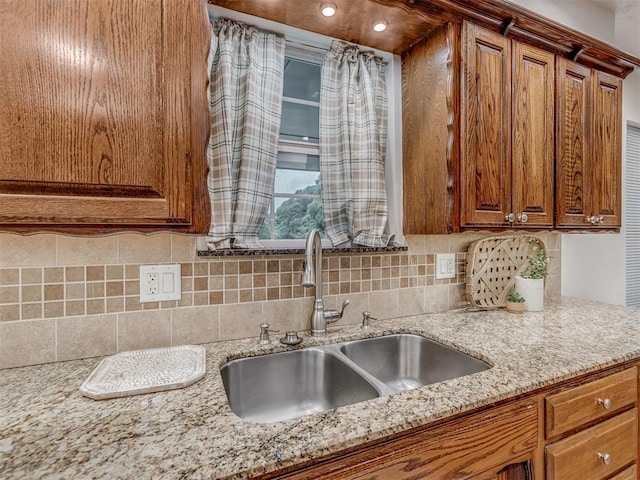 kitchen with a sink, light stone counters, decorative backsplash, and brown cabinetry