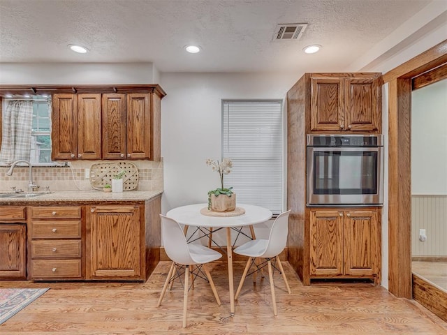 kitchen featuring visible vents, brown cabinetry, oven, a textured ceiling, and a sink