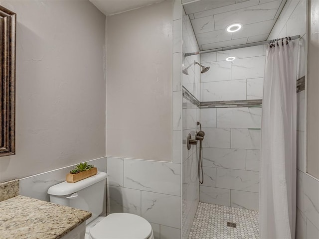 bathroom with wainscoting, vanity, toilet, tile walls, and tiled shower